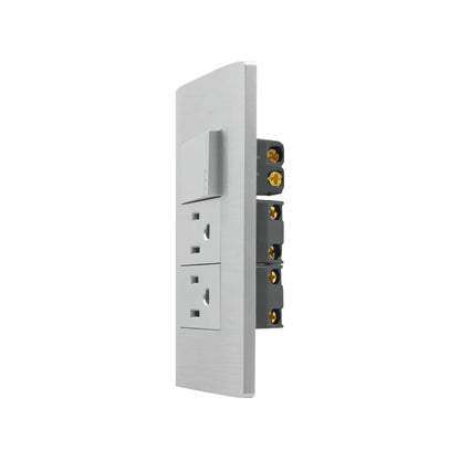 Placa eléctrica de pared gris con 1 interruptor de luz y 2 tomas de corriente, vista lateral con terminales dorados.